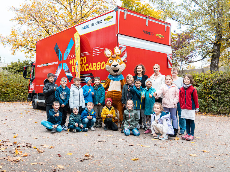 Mascotte Blicki samen met kinderen voor een rode vrachtwagen | © Humbaur GmbH