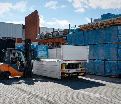 Een vorkheftruck wordt gebruikt om bouwmaterialen in een trailer te laden voor een bouwmarkt. | © Humbaur GmbH