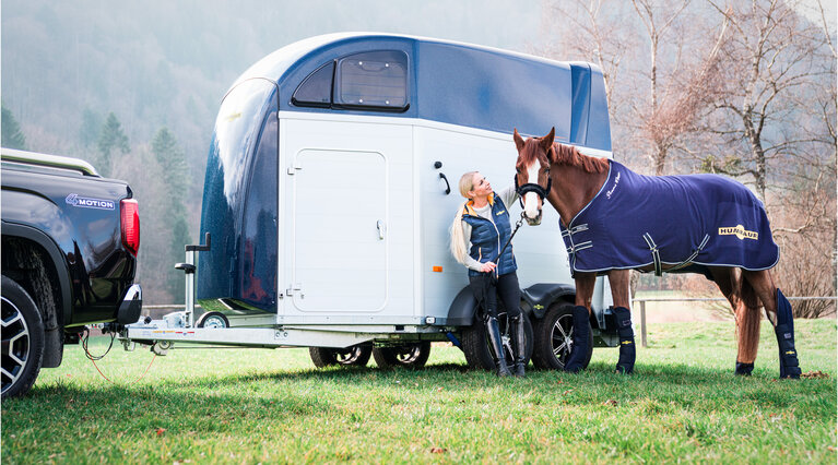 A lady is stroking her horse in front of the Equitos Alu.