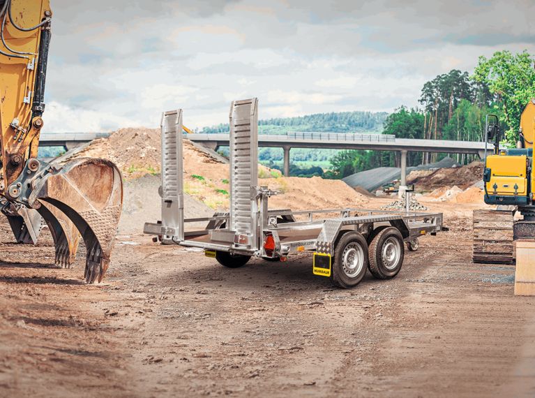 HS Basis,Un transporteur d'engins de chantier Humbaur équipé de rampes d'accès, stationné sur un chantier., à droite à l'avant | © Humbaur GmbH